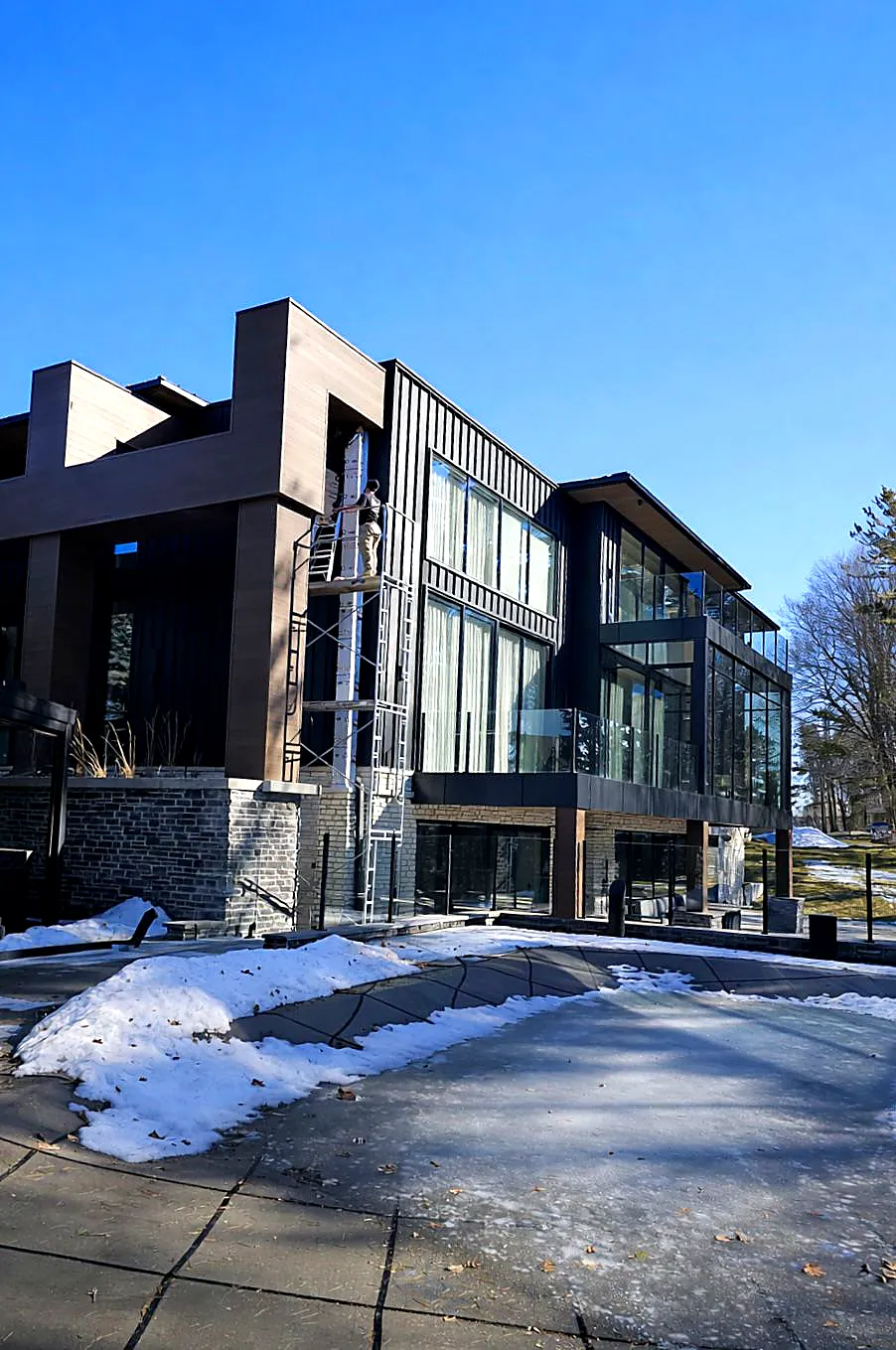 Modern three-storey home with black metal, wood-look panels and stone base