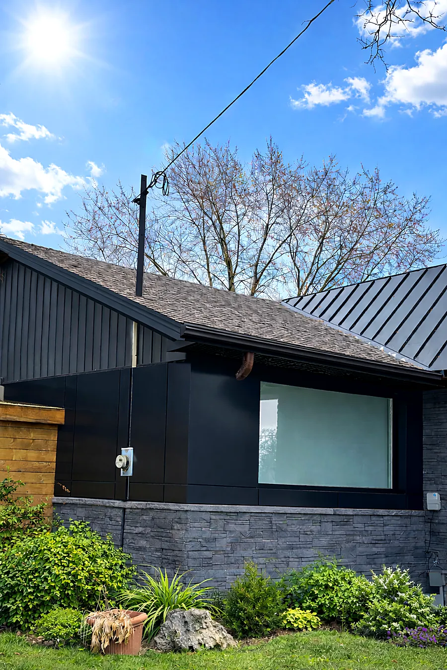 Bungalow with black panels, metal roof and stone veneer base